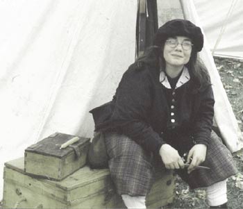 This is a picture of me, sitting on a wooden trunk at a Rendezvous event in Winona, Minnesota. I am in my 17th century soldiers uniform consisting of a Blue bonnet (sort of looks like a beret), Grey coat, plaid britches, wool socks and latchet shoes.